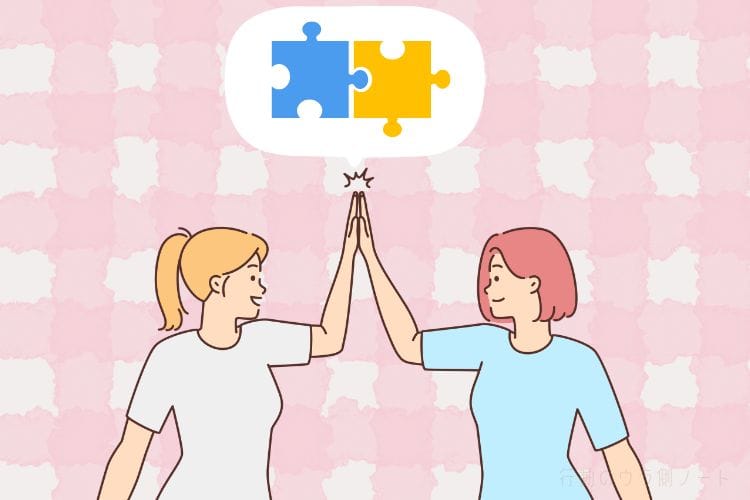 フラットなベクターイラスト。ピンクの格子模様が描かれた白い背景に、2人の若い女性が立っている。左の女性は金髪のポニーテールで白いTシャツ、右の女性はピンクのボブカットで水色のTシャツを着ている。2人は中央で笑顔でハイファイブ（ハイタッチ）をしている。その手の上に白い吹き出しがあり、中には合体した青と黄色のパズルピースが描かれている。右下隅には薄い日本のテキストで「行動のウラ側ノート」と配置されている。